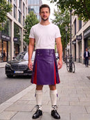 A man stands on a city sidewalk wearing a white crew-neck t-shirt and a purple leather kilt with red side panels, paired with white knee-high socks and black leather shoes. A Mercedes-Benz car and urban buildings are visible in the background.