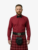 Man wearing a red shirt, bow tie, and tartan kilt on a white background