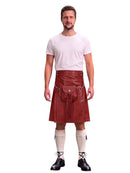 A man modeling a dark red leather kilt with a front pouch pocket, paired with a white t-shirt, cream knee-high socks, and black lace-up shoes, against a plain white background.