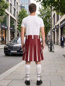 A man standing on a city sidewalk, viewed from behind, wearing a white t-shirt and a pleated red leather kilt with white vertical stripes, white knee-high socks, and black shoes.