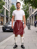 A man stands on a city sidewalk wearing a white crew-neck t-shirt, a dark red faux-leather kilt with white geometric stitching, white knee-high socks, and black leather shoes. The background shows a blurred street scene with a black Mercedes-Benz car, storefronts, and trees.