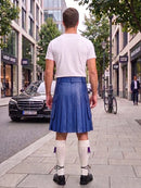 A man viewed from behind wearing a blue leather kilt, white t-shirt, white knee-high socks, and black shoes, standing on a city sidewalk.