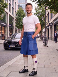 A man standing on a city sidewalk wearing a blue leather kilt, white t-shirt, white knee-high socks, and black shoes, with storefronts, trees, and a parked car in the background.