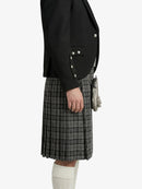 Person wearing a black blazer with studded details and a plaid skirt on a white background