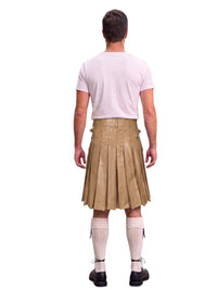 A man shown from the back wearing a light pink t-shirt, a tan pleated leather kilt, white knee-high socks, and black shoes, against a solid white background.